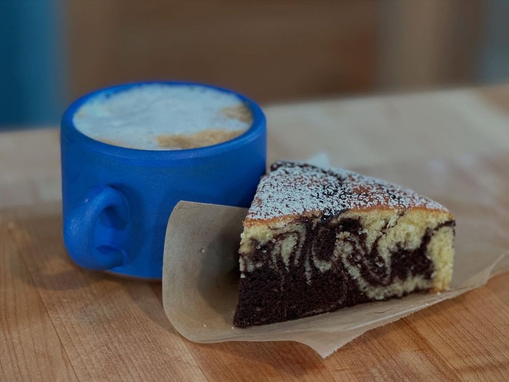 Latte in a blue mug beside a slice of cake